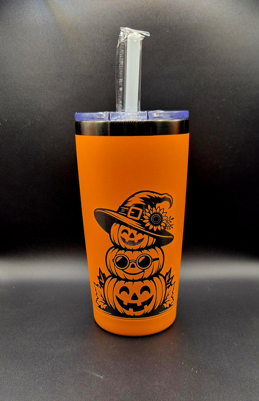 Bright orange 20 oz stainless steel Halloween tumbler with black laser-engraved artwork of three stacked smiling jack-o'-lantern pumpkins, round glasses, autumn leaves, and a witch hat decorated with a sunflower. Clear lid and straw included.