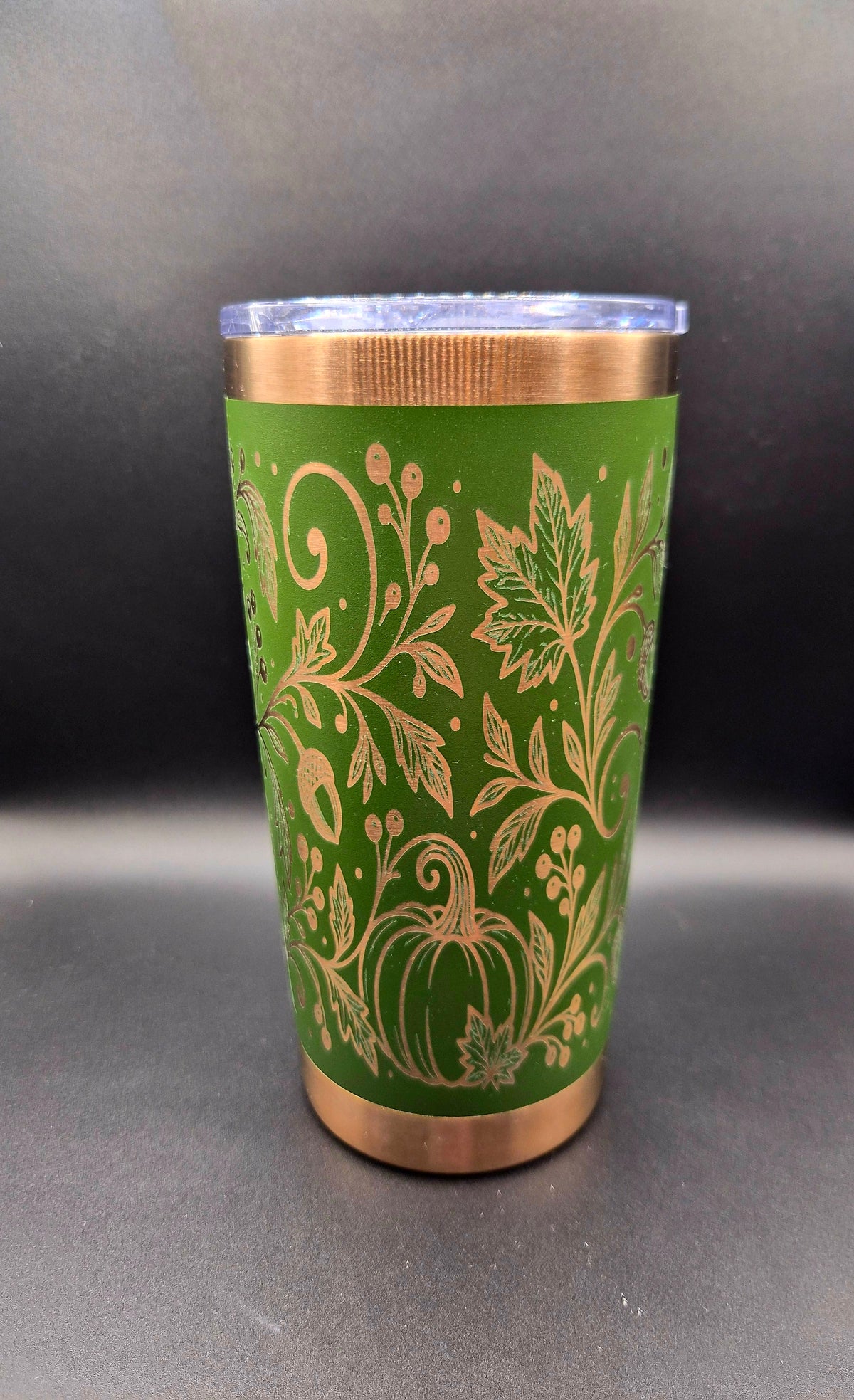 Green 20 oz stainless steel tumbler with copper accents and intricate laser-engraved autumn design featuring pumpkins, swirling vines, fall leaves, and acorns.