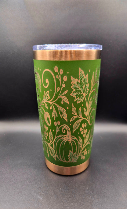 Green 20 oz stainless steel tumbler with copper accents and intricate laser-engraved autumn design featuring pumpkins, swirling vines, fall leaves, and acorns.