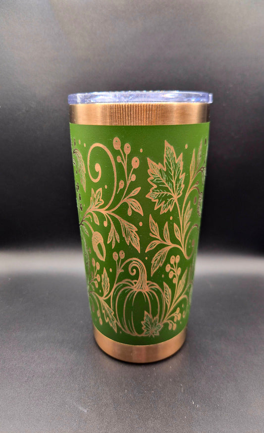 Green 20 oz stainless steel tumbler with copper accents and intricate laser-engraved autumn design featuring pumpkins, swirling vines, fall leaves, and acorns.