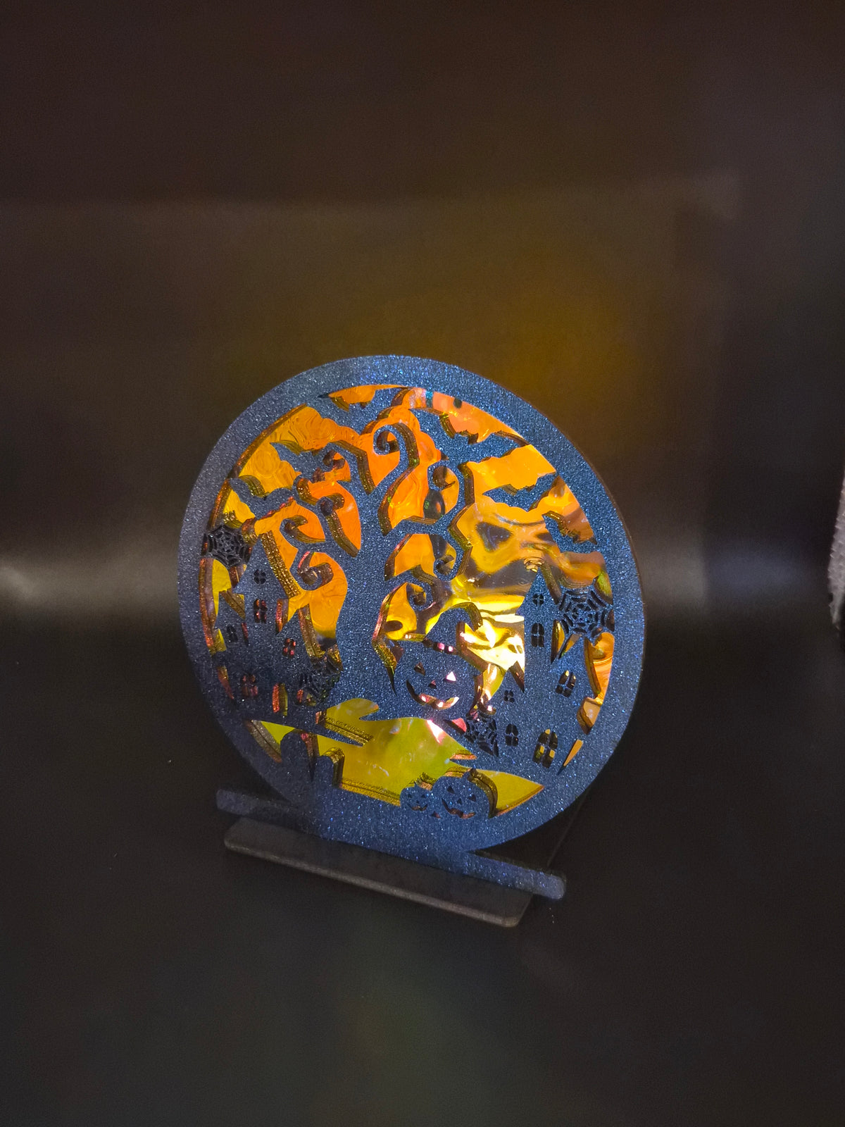 Backlit Halloween tabletop decoration featuring haunted houses, bats and a spooky tree silhouetted against glowing orange iridescent backing.