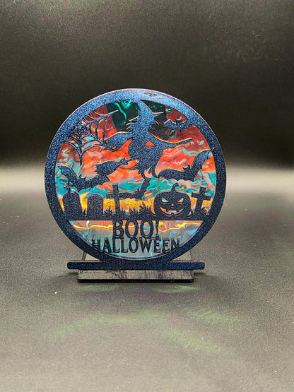 Round Halloween decoration featuring bats, gravestones, jack-o'-lantern and BOO HALLOWEEN lettering over an iridescent background.