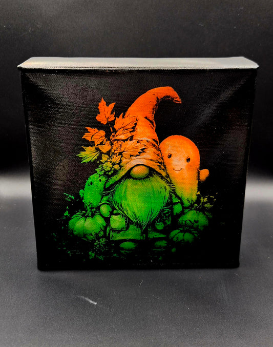Laser-engraved Halloween mini canvas featuring a green and orange gnome in a witch hat with a friendly ghost, pumpkins and autumn leaves on a black background.