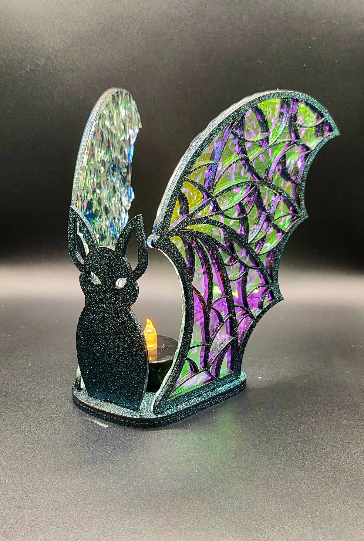 Handcrafted Halloween bat LED tealight holder with black bat silhouette, purple and green iridescent acrylic wings and a glowing tealight.
