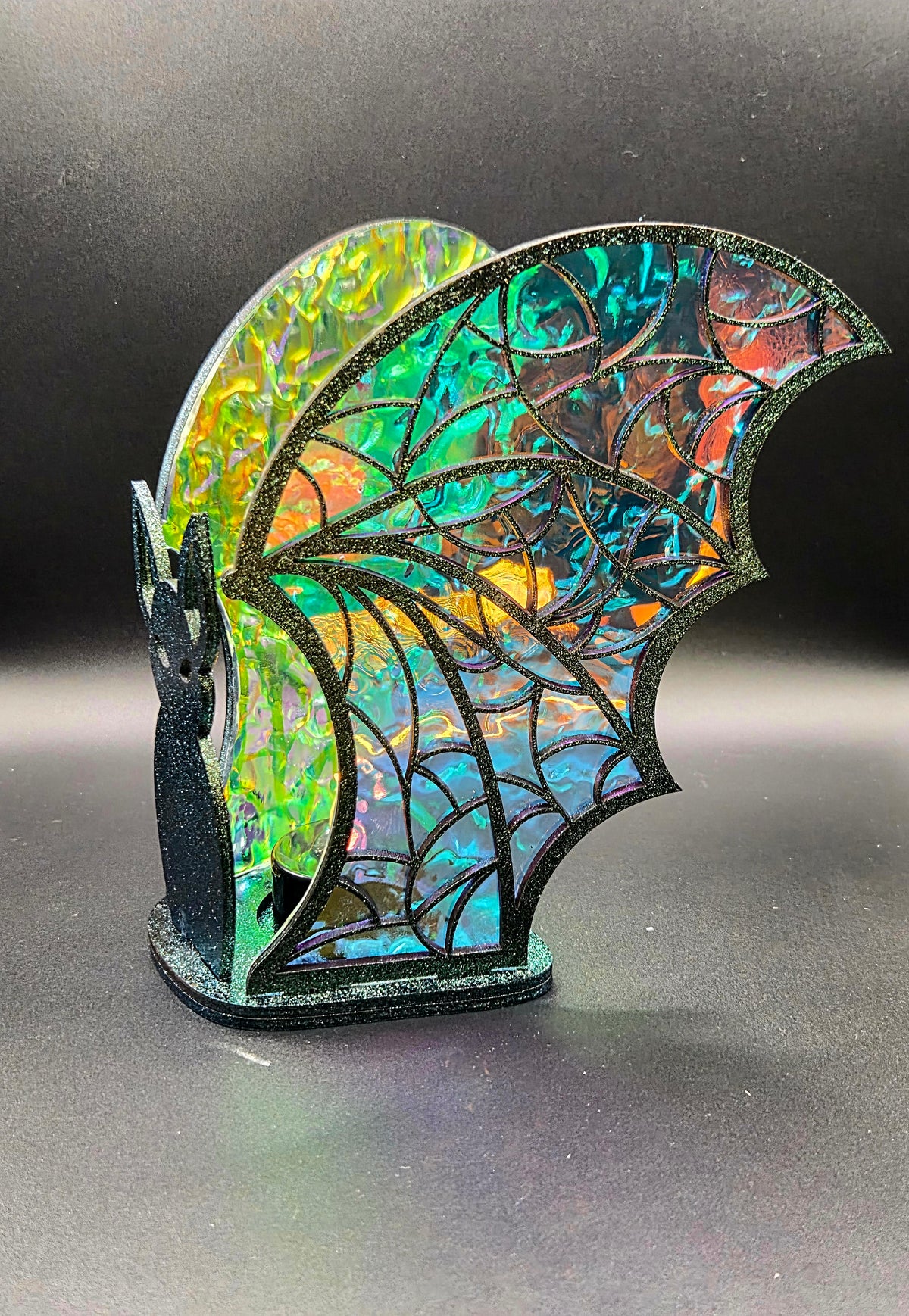Side view of iridescent bat tealight decoration showing intricate black web-patterned wings with turquoise, orange and green reflections.