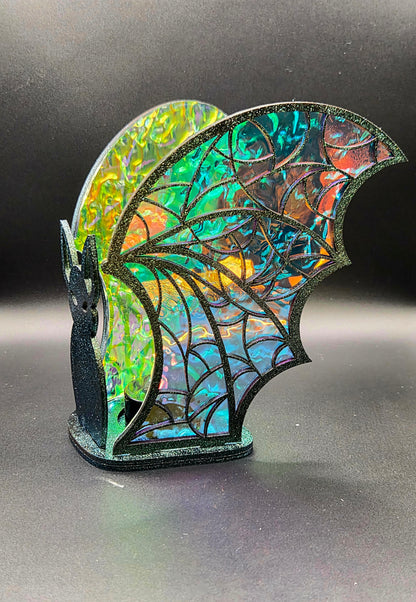 Side view of iridescent bat tealight decoration showing intricate black web-patterned wings with turquoise, orange and green reflections.