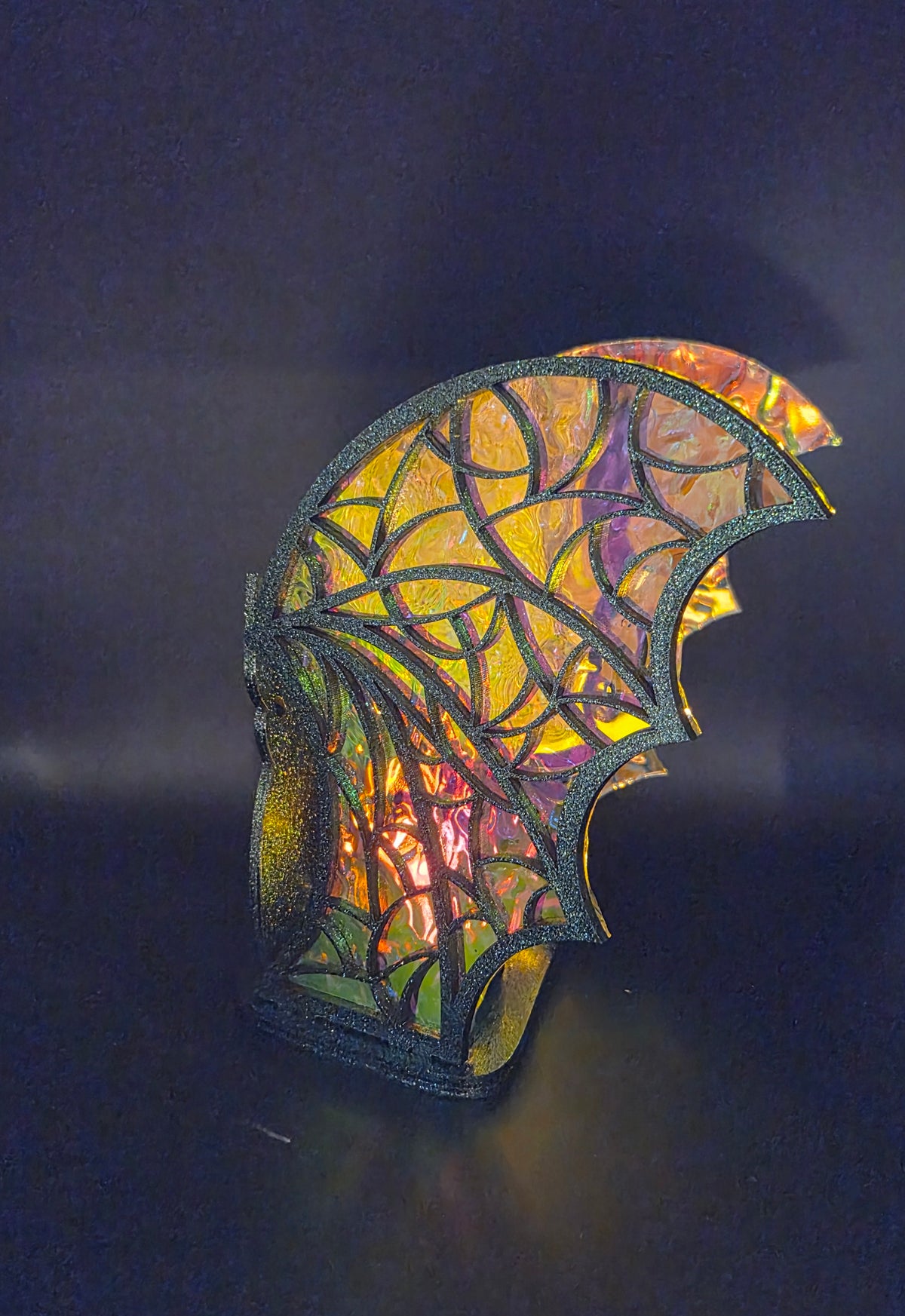 Close-up of illuminated bat tealight holder wings with stained-glass-style web patterns and shimmering golden and purple acrylic.