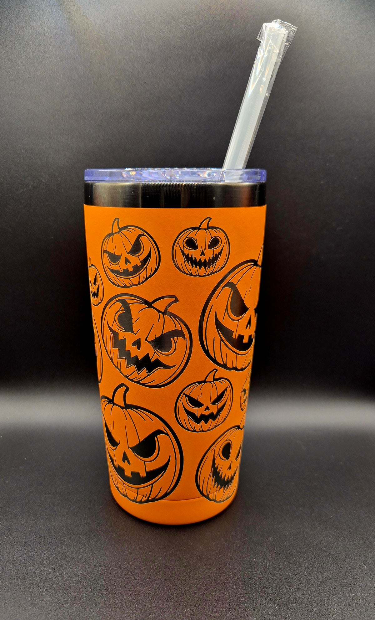 Bright orange stainless steel Halloween tumbler with black laser-engraved jack-o'-lantern faces in assorted sizes and expressions.