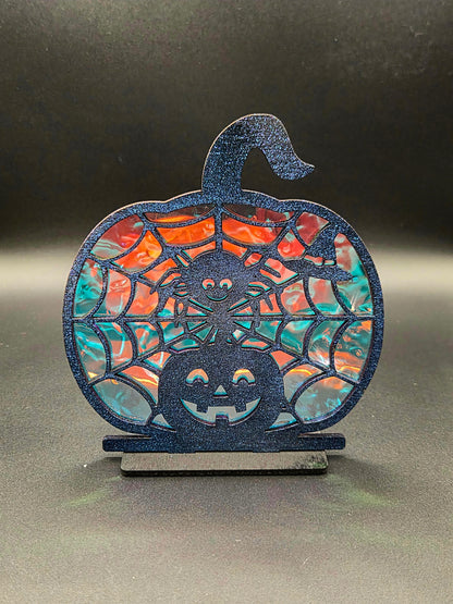 Pumpkin-shaped Halloween decoration with smiling spider, spiderwebs and jack-o'-lantern against orange and turquoise iridescent backing.