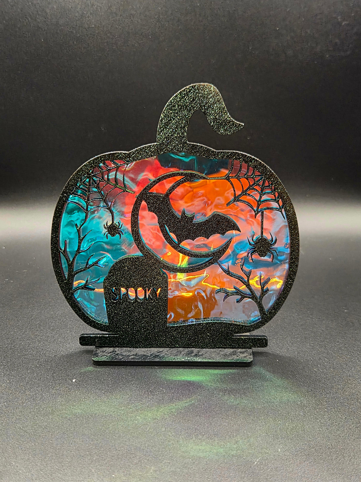 Pumpkin-shaped Halloween tabletop decoration featuring a crescent moon, bat, spiders and SPOOKY gravestone with iridescent backing.