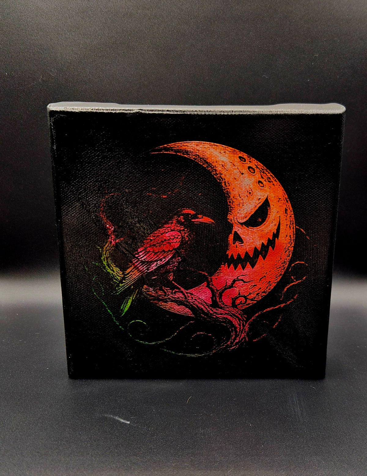 Gothic Halloween laser-engraved canvas featuring a raven perched on twisting branches beneath a sinister orange crescent moon, with crimson and green details against a black background.