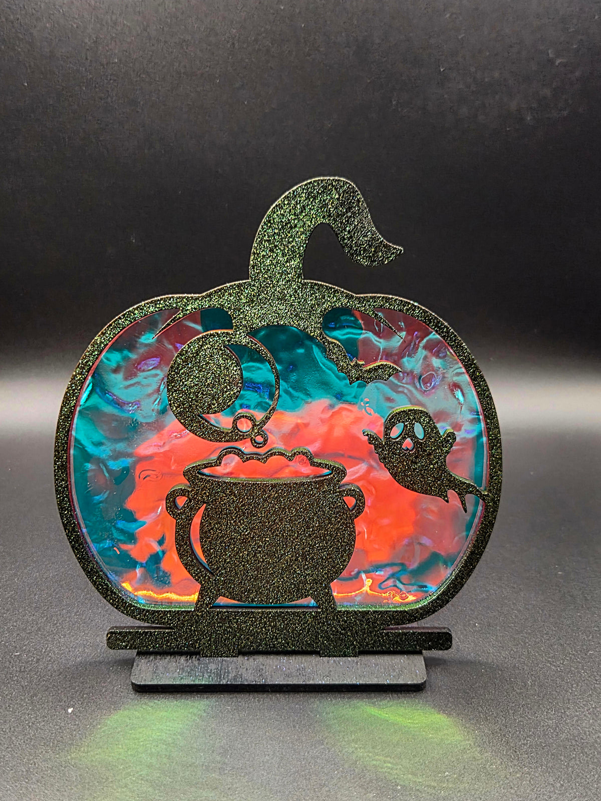 Pumpkin-shaped Halloween tabletop decoration featuring black bubbling cauldron, friendly ghost and colorful iridescent backing.