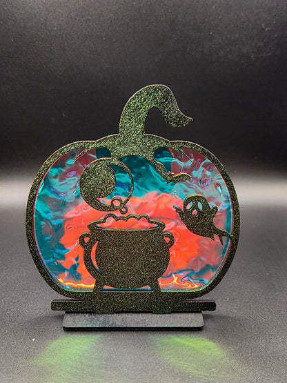 Pumpkin-shaped Halloween tabletop decoration featuring black bubbling cauldron, friendly ghost and colorful iridescent backing.